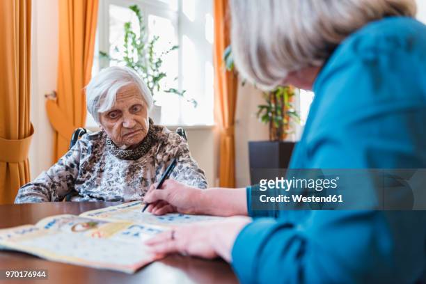 woman taking care of old woman doing crossword puzzle - crossword stock pictures, royalty-free photos & images