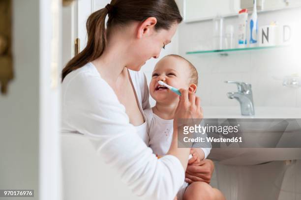 mother brushing baby's teeth in bathroom - mother and baby taking a bath stock pictures, royalty-free photos & images
