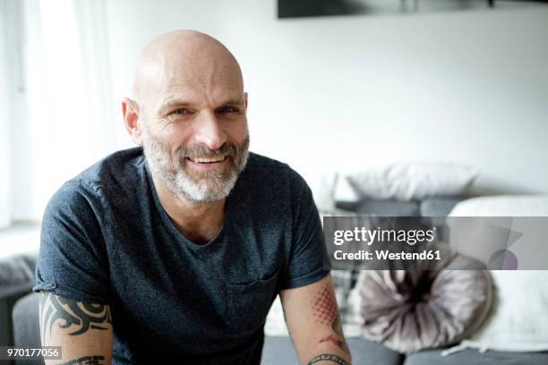 tattooed man at home sitting on couch - glatze mann stock-fotos und bilder