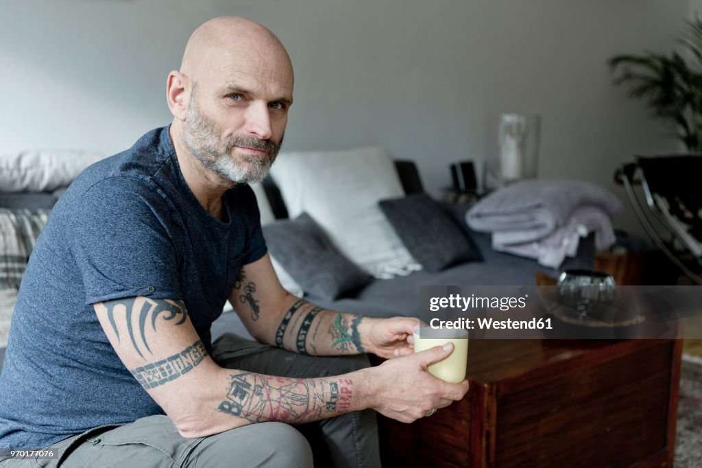 Tattooed man at home sitting on couch, drinking coffee