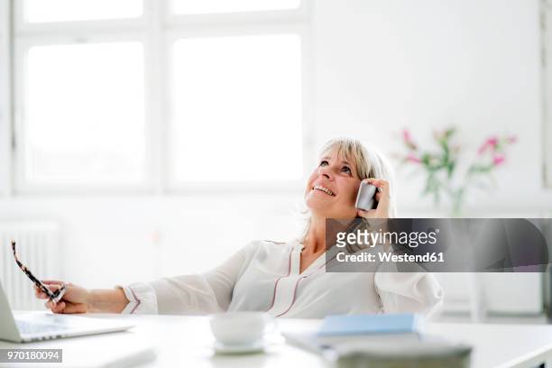 happy mature businesswoman on cell phone at desk - white blouse stock-fotos und bilder