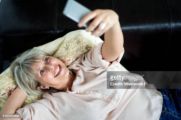 happy mature woman lying down holding cell phone - down blouse ストックフォトと画像