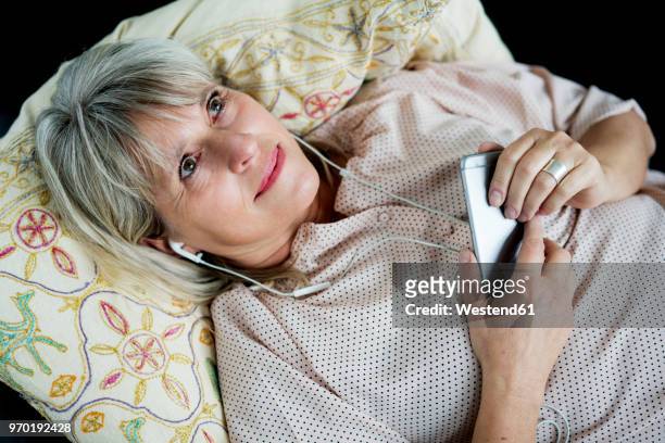 smiling mature woman lying down with cell phone and earphones - down blouse imagens e fotografias de stock