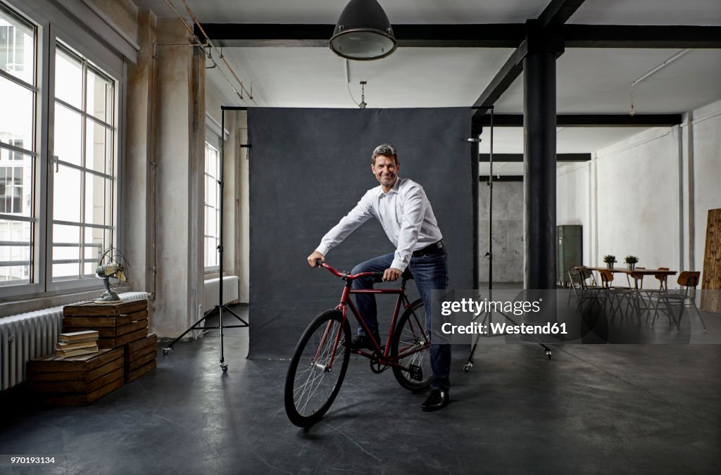 Portrait of mature businessman on fixie bike in front of black backdrop in loft