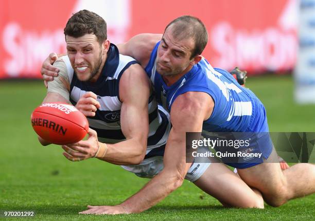 Sam Menegola of the Cats handballs whilst being tackled by Ben Cunnington of the Kangaroos during the round 12 AFL match between the Geelong Cats and...