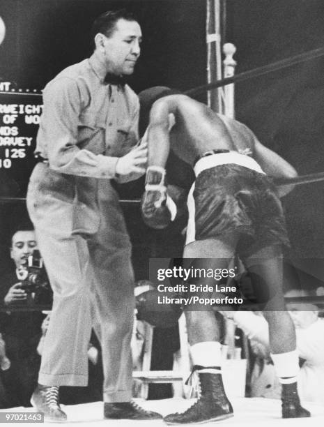 Referee George Latka holds up American world featherweight champion Davey Moore after he was knocked down in the tenth round by Cuban challenger...