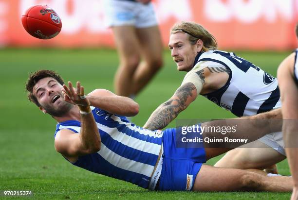 Luke McDonald of the Kangaroos handballs whilst being tackled by Tom Stewart of the Cats during the round 12 AFL match between the Geelong Cats and...