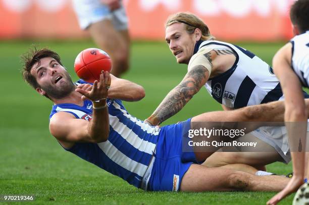 Luke McDonald of the Kangaroos handballs whilst being tackled by Tom Stewart of the Cats during the round 12 AFL match between the Geelong Cats and...