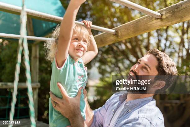 father supporting daughter hanging on monkey bars - jungle gym stock pictures, royalty-free photos & images