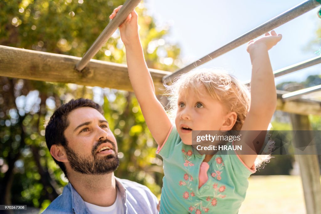 Father looking at daughter climbing monkey bars