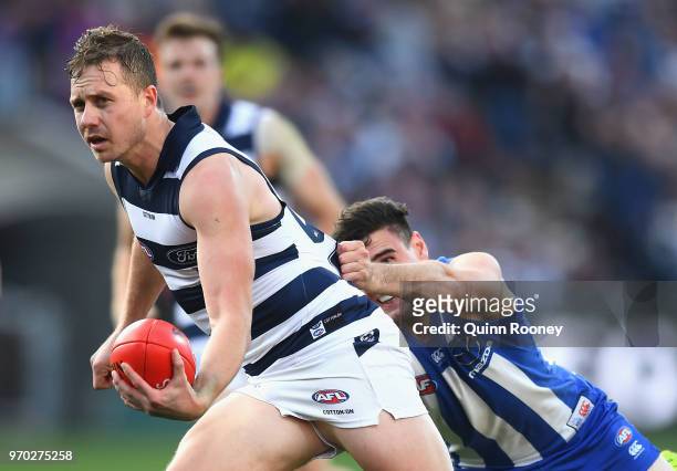 Mitch Duncan of the Cats handballs whilst being tackled during the round 12 AFL match between the Geelong Cats and the North Melbourne Kangaroos at...