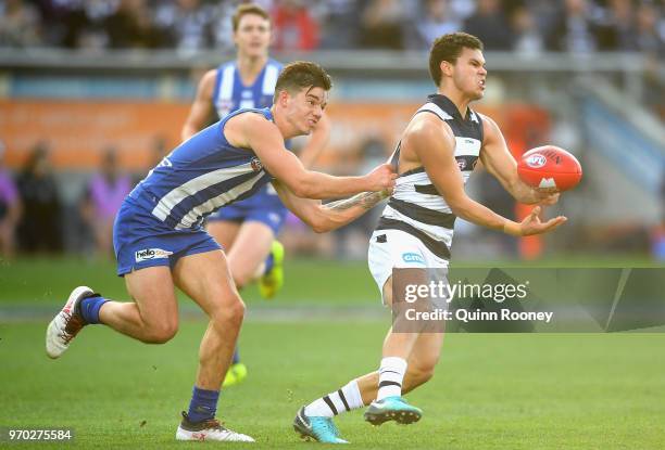 Brandan Parfitt of the Cats handballs whilst being tackled by Jy Simpkin of the Kangaroos during the round 12 AFL match between the Geelong Cats and...