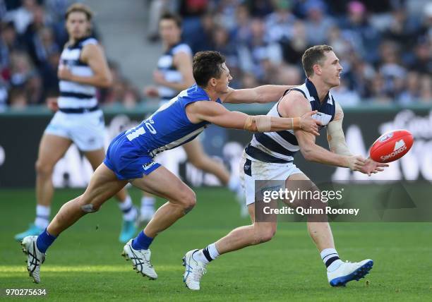 Joel Selwood of the Cats handballs whilst being tackled by Ben Jacobs of the Kangaroos during the round 12 AFL match between the Geelong Cats and the...