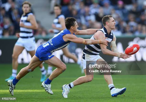 Joel Selwood of the Cats handballs whilst being tackled by Ben Jacobs of the Kangaroos during the round 12 AFL match between the Geelong Cats and the...