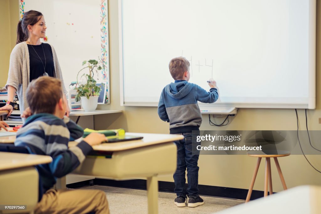 Young boy writing on interactive whiteboard in classroom.