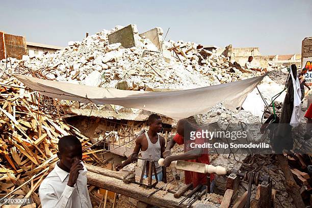 With a collapsed hotel in the background, a carpenter fashions a bedpost at an improvised sawmill near where the collapsed Marche Tete Boeuf market...