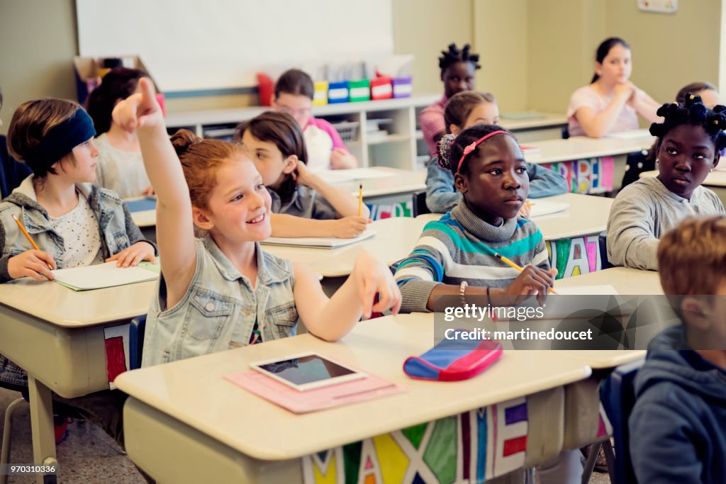 Elementary school children with arms raised in classroom.