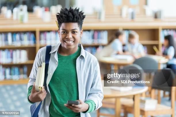 confident teenage boy checks books out from the library - book standing on end stock pictures, royalty-free photos & images