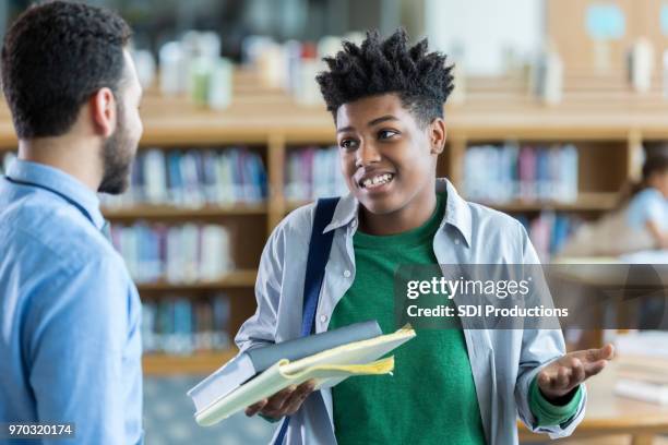 männlichen high-school-schüler mit lehrer und zuckt mit den schultern steht - book standing on end stock-fotos und bilder