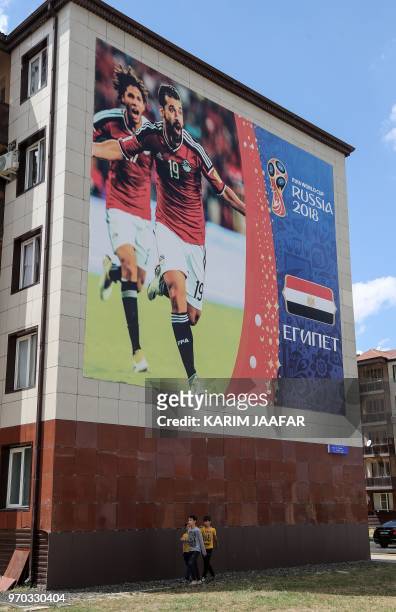 Children walk in front of a giant poster featuring Egypt's footballers Abdalla Said and Mohamed Elneny attached to the wall of a residential building...