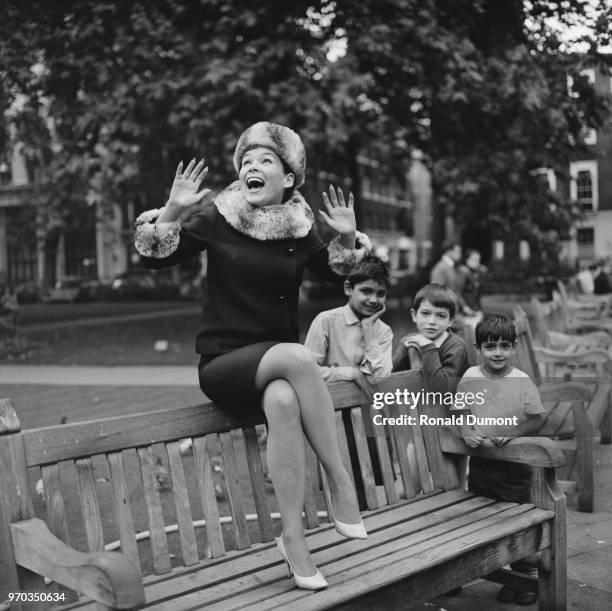 American actress and ballet dancer Yvonne Craig sitting on a bench while three children stand in the background, UK, 20th September 1967. She is...