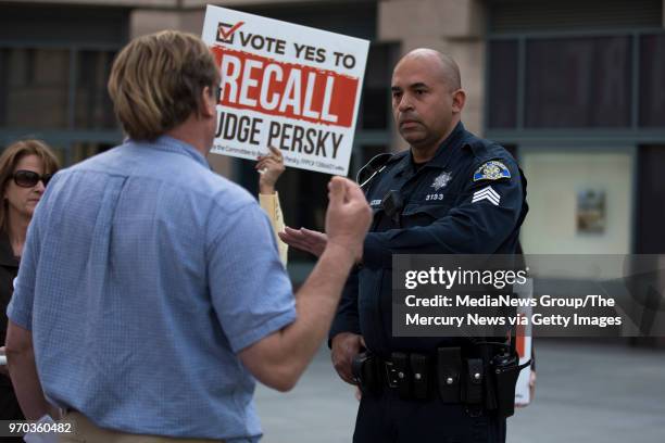 Steve White, left, who came in opposition of a recall, is asked by an officer to step back from speakers at a recall rally outside of attorney James...