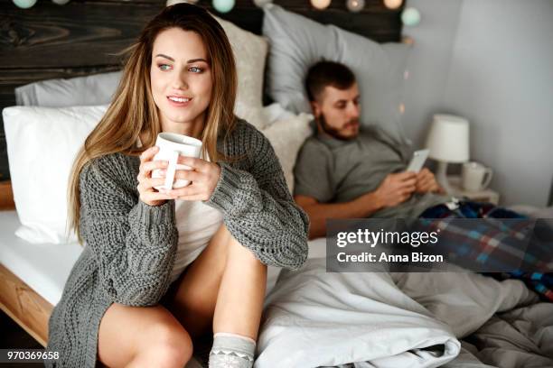 woman sitting with coffee and man on phone in bedroom. debica, poland - lazy poland stock pictures, royalty-free photos & images