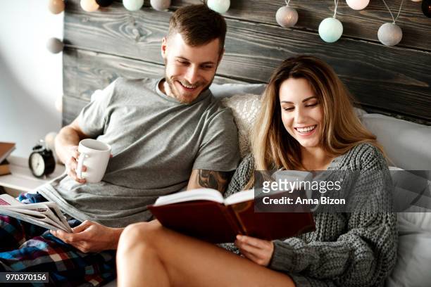 happy young couple with coffee reading in bed. debica, poland - lazy poland stock pictures, royalty-free photos & images