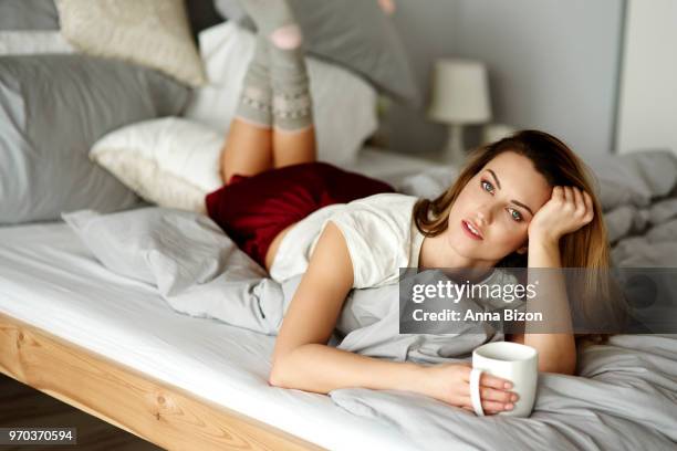 dreamy woman with coffee lying on stomach in bedroom. debica, poland - lazy poland stock pictures, royalty-free photos & images