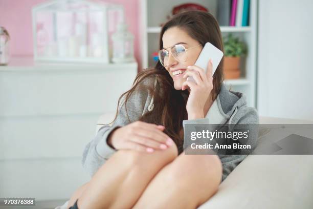 shot of woman sitting on couch wearing hoodie while talking on the phone. debica, poland - anna bizon foto e immagini stock