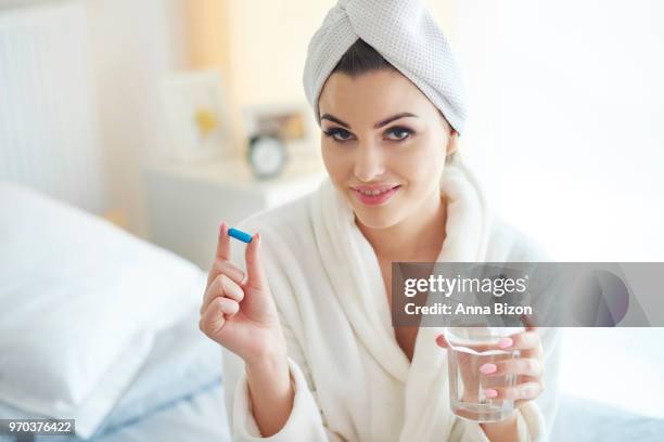 woman sitting in bathrobe, holding pill and glass of water. debica, poland - anna bizon stock pictures, royalty-free photos & images