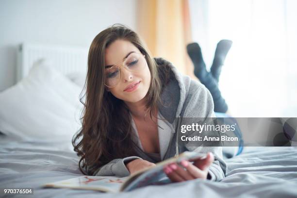 woman lying on stomach on top of bed while reading. debica, poland - anna bizon stock pictures, royalty-free photos & images