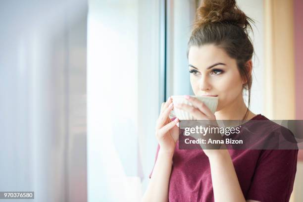 woman drinking coffee indoors, looking out the window. debica, poland - anna bizon stock pictures, royalty-free photos & images