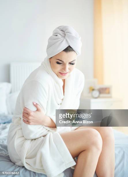 woman sitting in bath robe on bed, holding stomach. debica, poland - bath robe stockfoto's en -beelden
