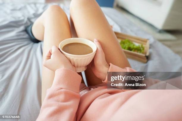 woman sitting in bed wearing pink jersey, holding mug of coffee. debica, poland - anna bizon foto e immagini stock