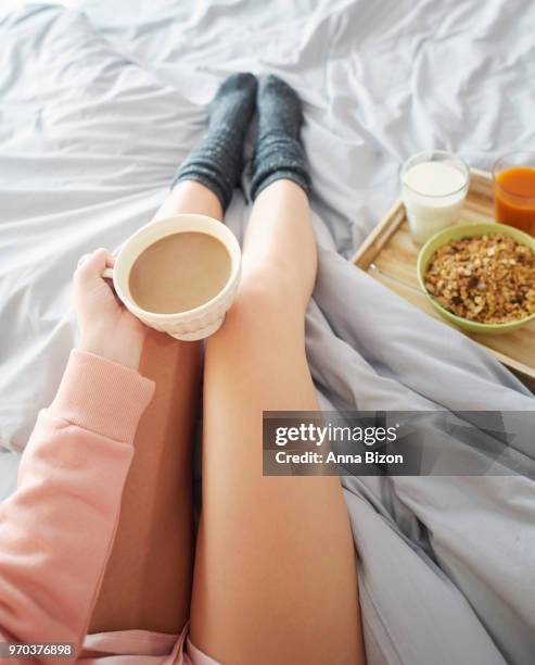 top view of woman's legs, sitting in bed, holding coffee with breakfast tray on the side. debica, poland - anna bizon foto e immagini stock