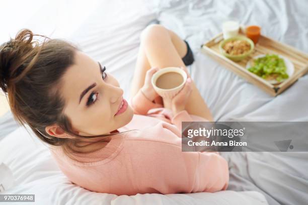 over the shoulder shot of woman sitting in bed with breakfast, looking back at camera. debica, poland - anna bizon stock pictures, royalty-free photos & images