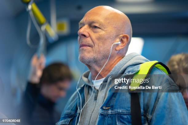 senior man listening to earphones on public transport - listening to podcast stock pictures, royalty-free photos & images