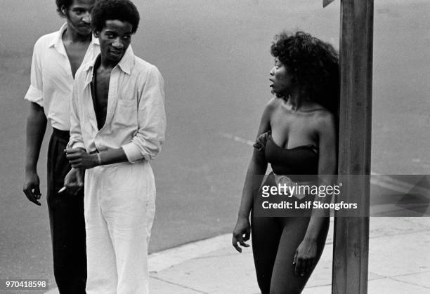 Elevated view of a pair of men as they stare at an unidentified woman in a lyrca bodysuit as she leans against a lamp pole, Washington DC, 1982.