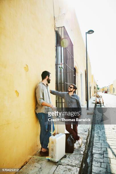 Smiling gay couple standing on street in discussion while exploring small town during vacation