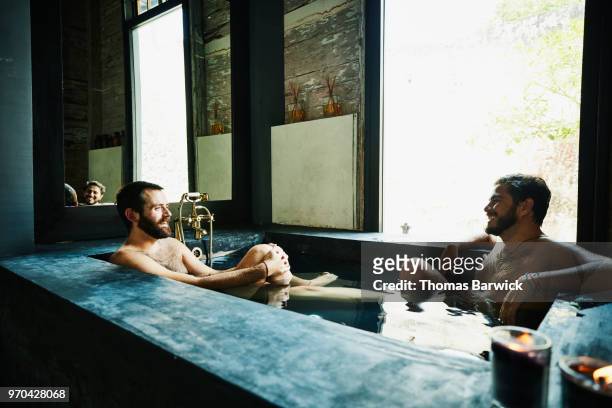smiling gay couple enjoying bath together in hotel spa - bad relationship stockfoto's en -beelden