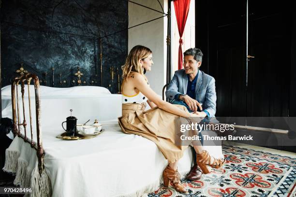 smiling couple in discussion while sitting on bed in boutique hotel before going out - fato castanho imagens e fotografias de stock