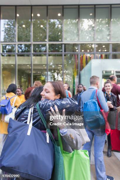 Female college students with bags hugging outside building