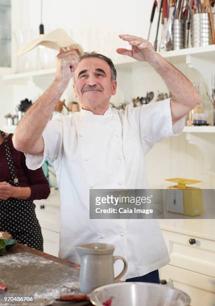 playful senior chef tossing pizza dough in kitchen - pizza toss foto e immagini stock