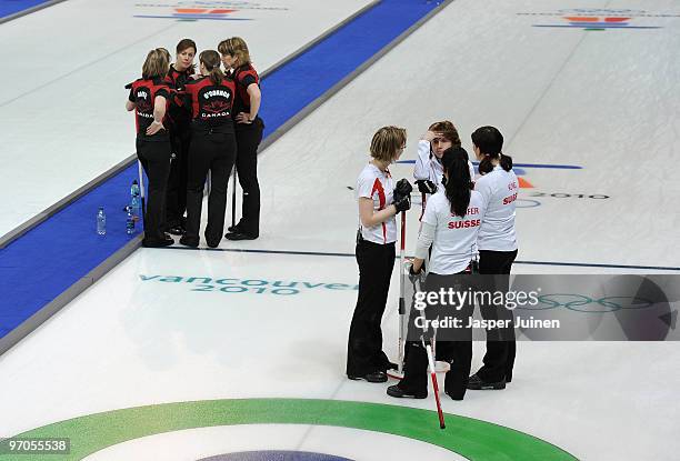 Skip Mirjam Ott of Switzerland chats with her teammates backdropped by the Canadian curling team during the women's curling semi-final game between...