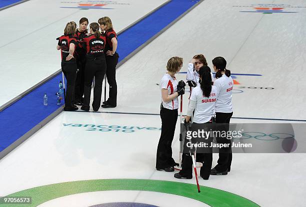 Skip Mirjam Ott of Switzerland chats with her teammates backdropped by the Canadian curling team during the women's curling semi-final game between...