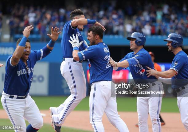 Luke Maile of the Toronto Blue Jays is congratulated by Gio Urshela and teammates after drawing a bases-loaded RBI walk to drive in the game-winning...