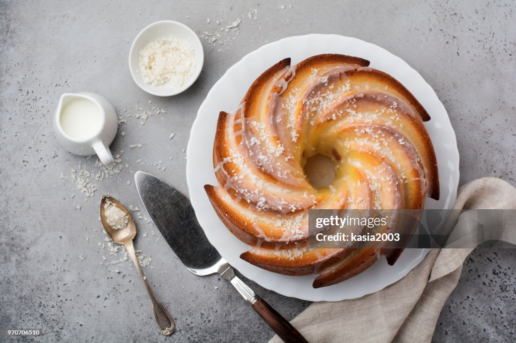 Bundt cake with sugar glaze and coconut on dark grey old concrete background. Selective focus. Top view with copy space.