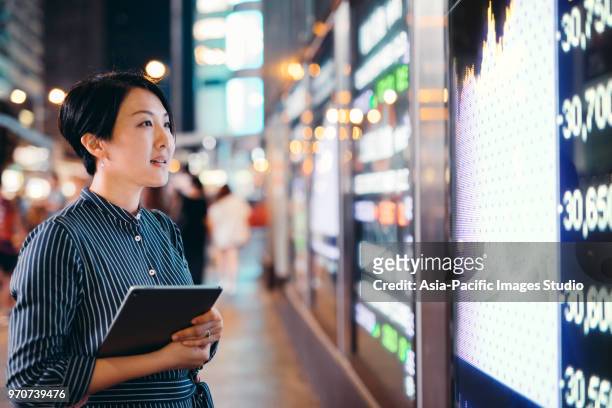 asian businesswomen checking stock market data on tablet before hong kong financial display board - china stock pictures, royalty-free photos & images