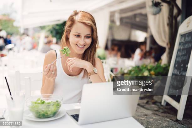 woman on summer vacation eating in restaurant and working on laptop - weight loss journey stock pictures, royalty-free photos & images